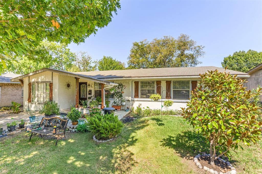 1801 Pleasant Run Road, Carrollton, TX 75006 Single-story residence featuring a painted masonry exterior, horizontal window shutters, covered front porch, and expansive front yard with mature landscaping