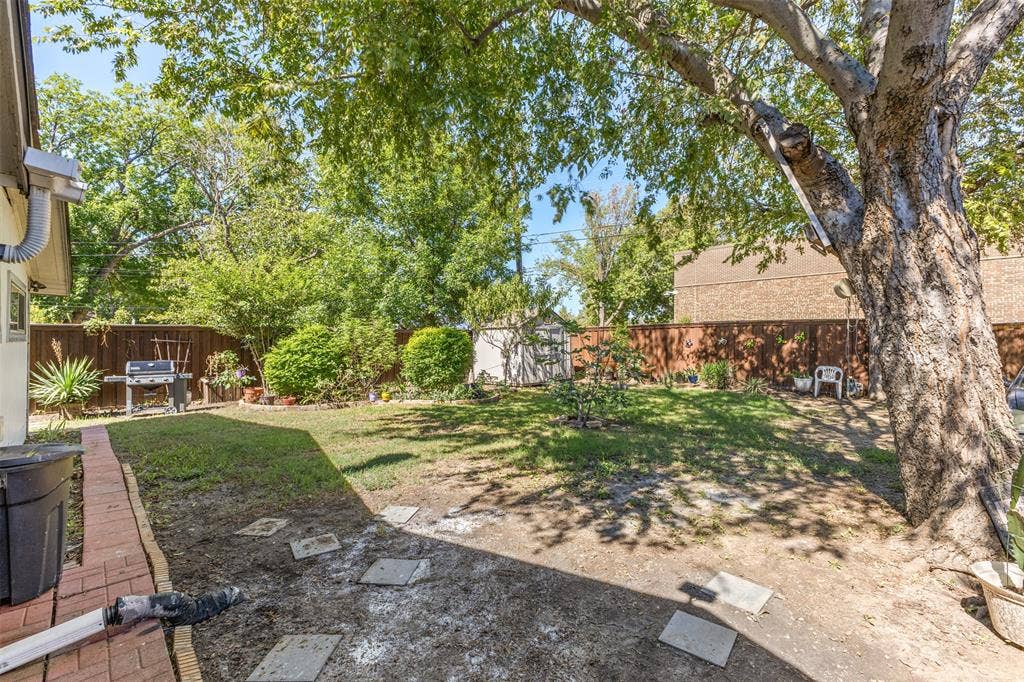 1801 Pleasant Run Road, Carrollton, TX 75006 Backyard featuring a wood privacy fence, mature trees, a brick walkway, and a detached storage shed