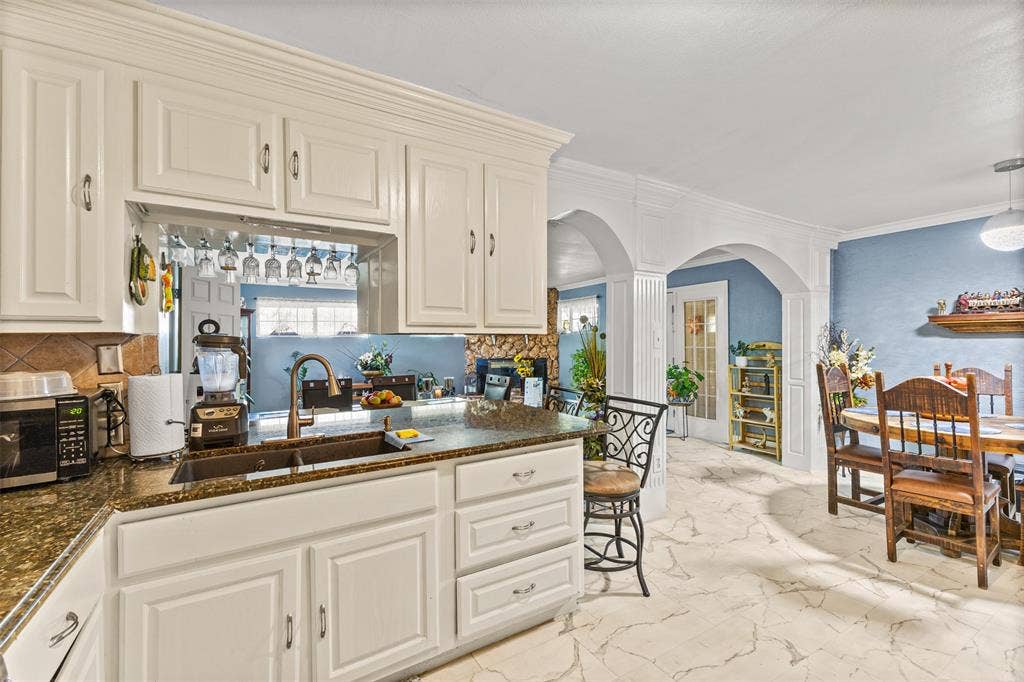 1801 Pleasant Run Road, Carrollton, TX 75006 White cabinetry, stone countertops, dual-basin sink, stone tile flooring, and decorative archways