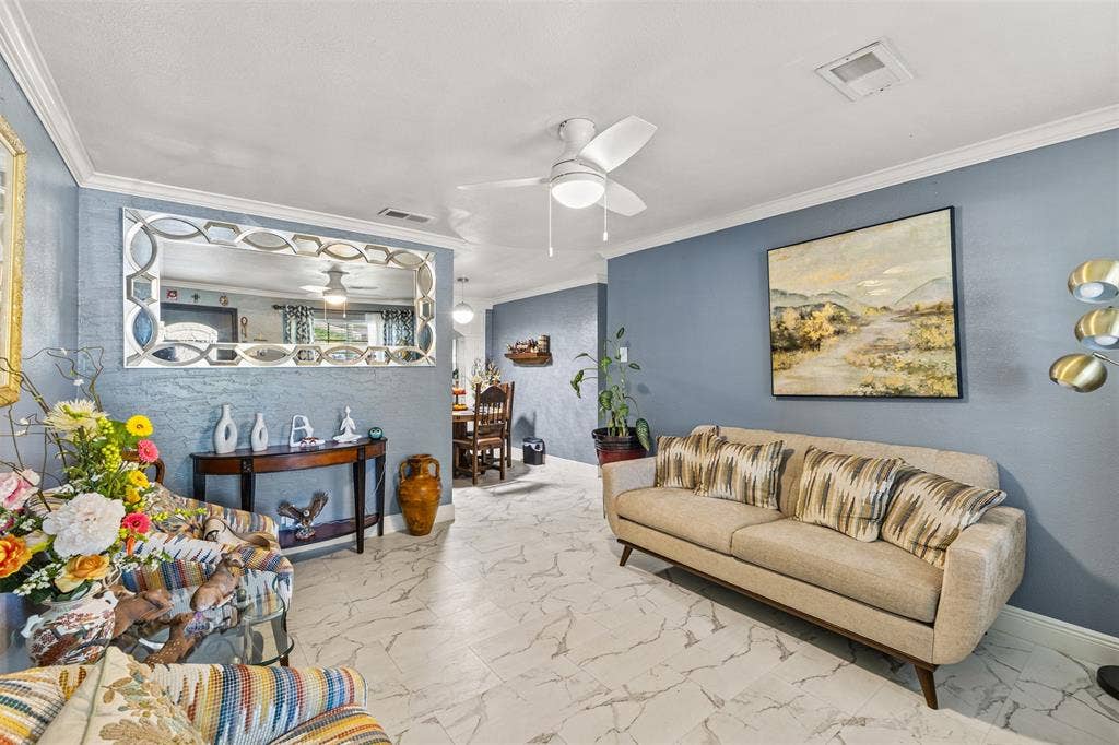 1801 Pleasant Run Road, Carrollton, TX 75006 Living area featuring stone-finish tile flooring, crown molding, and a central ceiling fan with integrated lighting