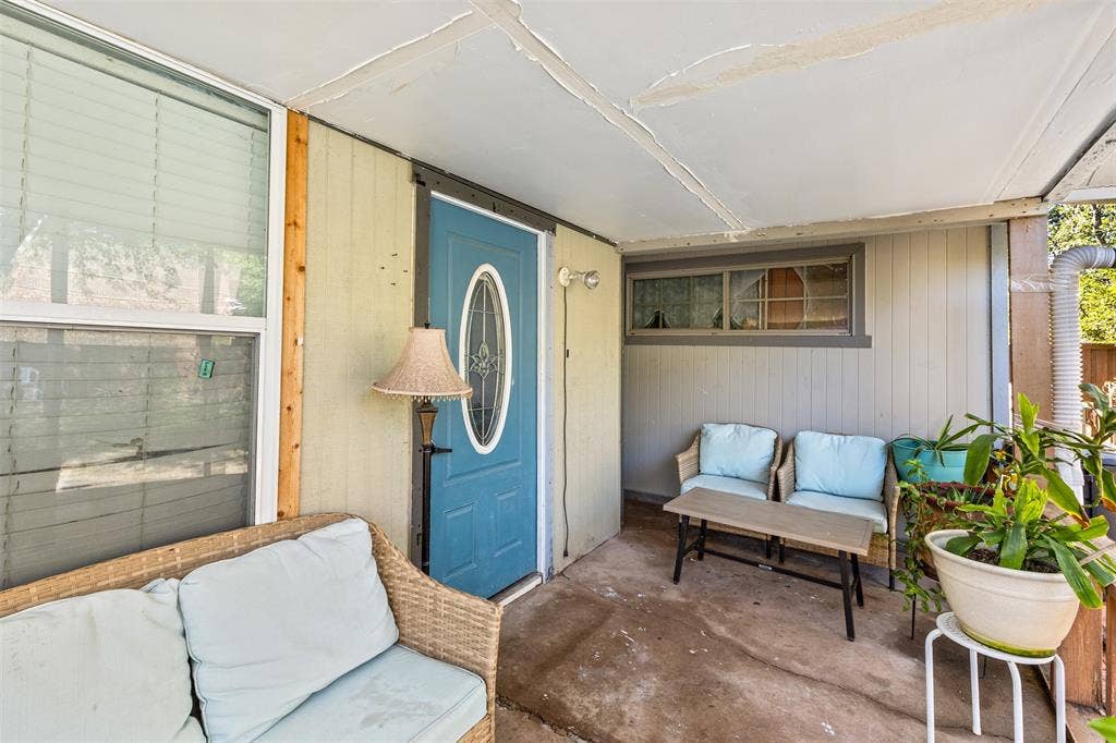 1801 Pleasant Run Road, Carrollton, TX 75006 Covered front porch featuring a concrete floor, horizontal and vertical wood-style siding, and a blue exterior door with a central oval glass insert