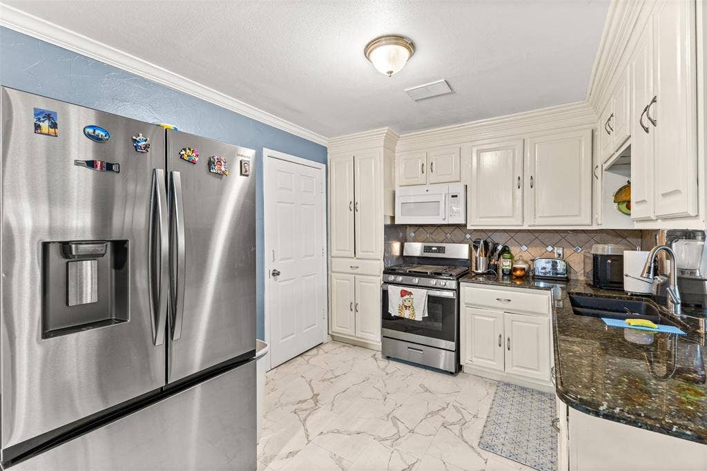 1801 Pleasant Run Road, Carrollton, TX 75006 Kitchen featuring white shaker-style cabinetry, stainless steel appliances, dark stone countertops, a tiled backsplash, and stone-finish tile flooring