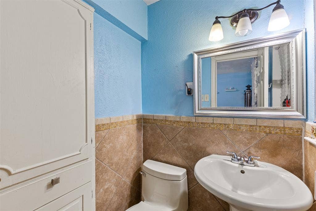 1801 Pleasant Run Road, Carrollton, TX 75006 Bathroom featuring a pedestal sink with a chrome faucet, large-format diamond-patterned wall tile with decorative accent border, built-in floor-to-ceiling cabinetry, and a framed vanity mirror with tri-light fixture