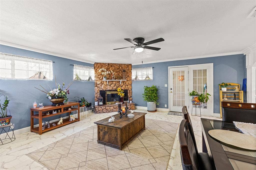 1801 Pleasant Run Road, Carrollton, TX 75006 Living area featuring natural stone fireplace surround, light-toned patterned tile flooring, ceiling fan, and multi-light glass pane exterior door