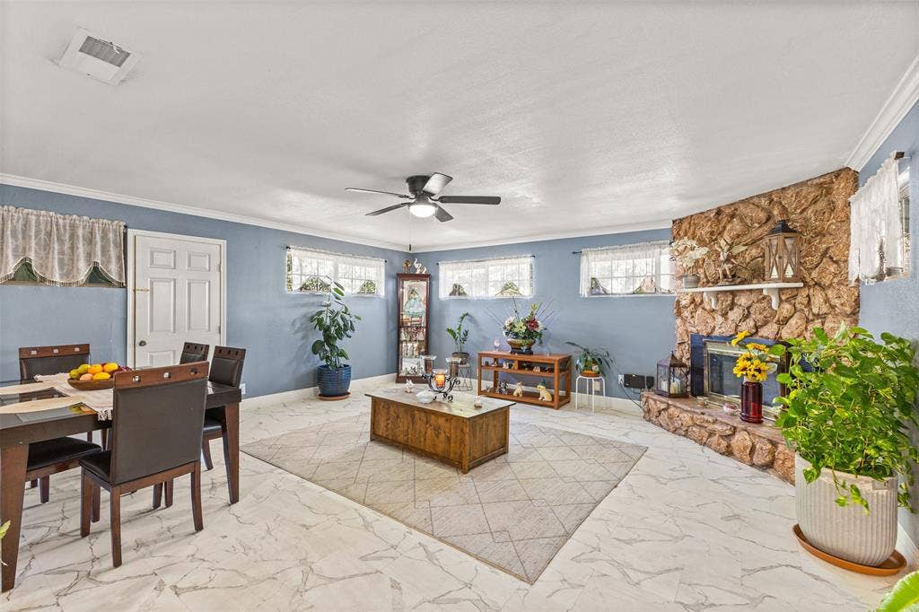 1801 Pleasant Run Road, Carrollton, TX 75006 Living area featuring large-format tile flooring, a floor-to-ceiling fieldstone fireplace with a mantel, crown molding, and a ceiling fan