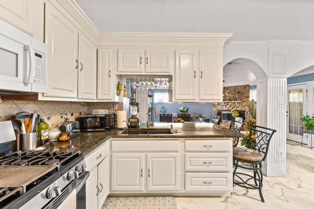1801 Pleasant Run Road, Carrollton, TX 75006 Kitchen featuring white cabinetry with crown molding, stone-finish countertops, stainless steel undermount sink with pull-down faucet, tile backsplash, and stone-finish flooring