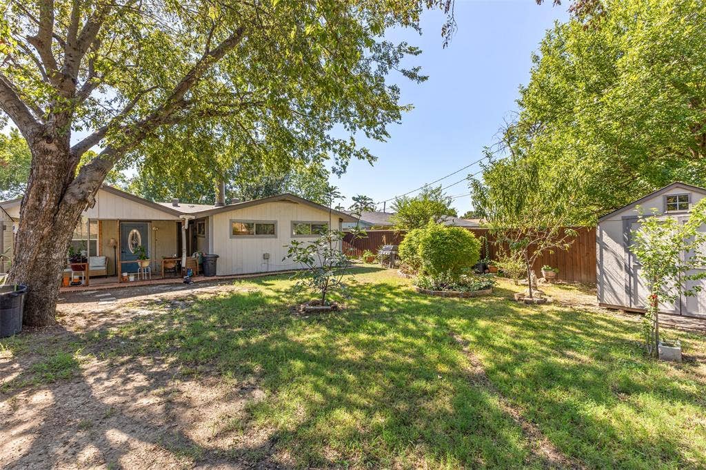 1801 Pleasant Run Road, Carrollton, TX 75006 Backyard featuring a covered patio, mature trees, wood privacy fencing, and a detached storage shed