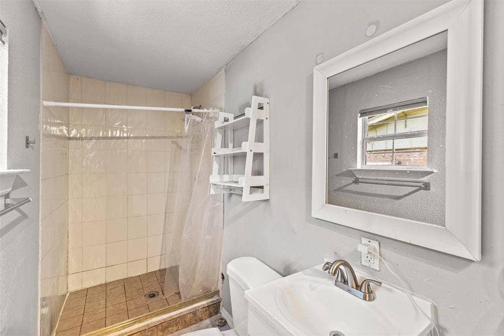 1801 Pleasant Run Road, Carrollton, TX 75006 Bathroom featuring a pedestal sink, metallic dual-handle faucet, tiled shower surround, square wall mirror, and built-in shelving