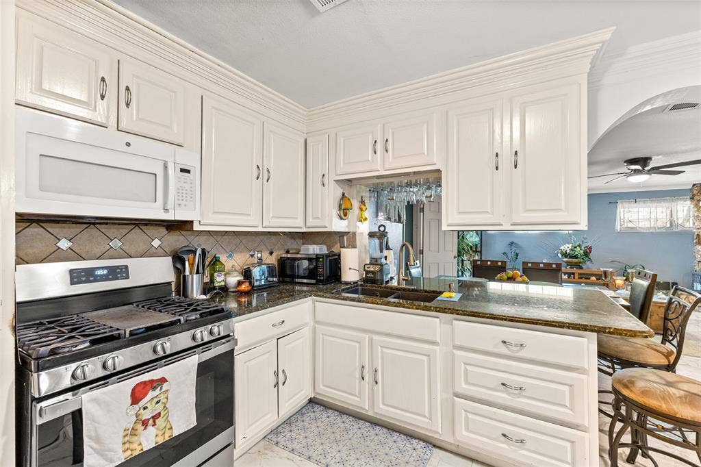 1801 Pleasant Run Road, Carrollton, TX 75006 Kitchen featuring white cabinetry with crown molding, stone-finish countertops, tile backsplash, built-in microwave, and a stainless steel gas range