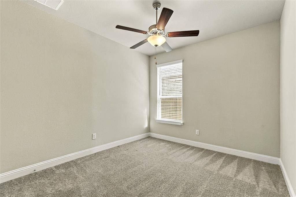 Neutral-toned walls, plush wall-to-wall carpeting, window with slatted blinds, and a central ceiling fan with integrated light fixture