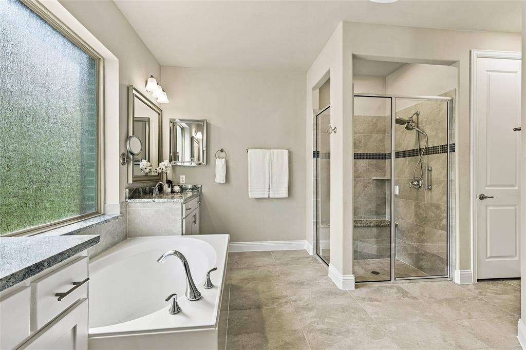Bathroom featuring a soaking tub with chrome fixtures, a separate glass-enclosed shower with tile surround, stone-top vanity, and large-format tile flooring