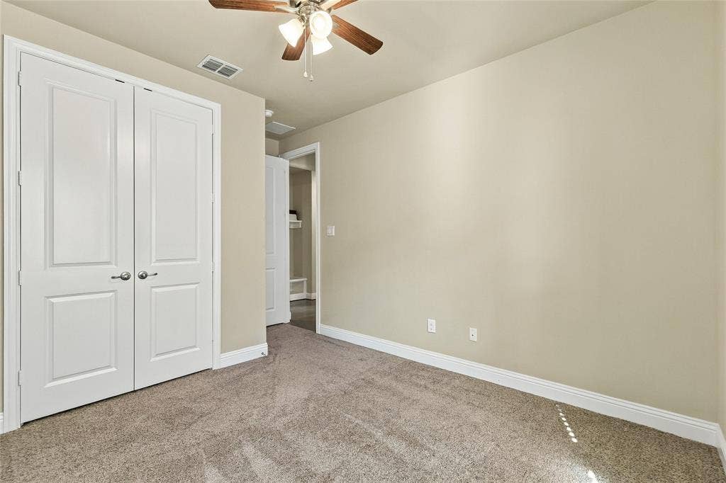 Neutral-toned walls, carpeted flooring, ceiling fan with integrated lighting, and double-panel closet doors
