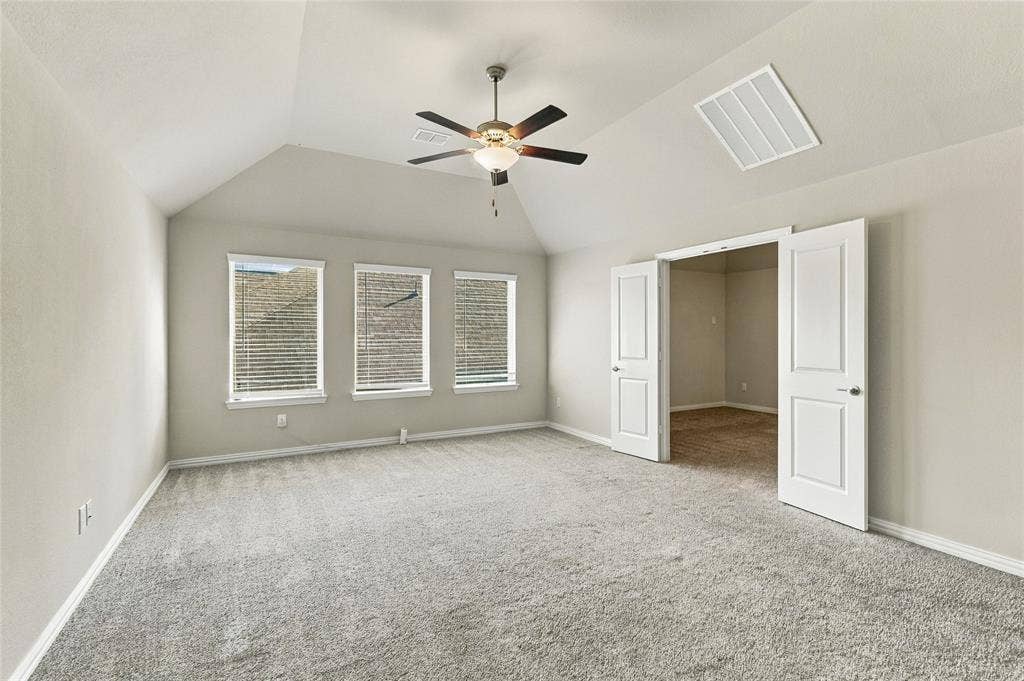 Vaulted ceiling room featuring neutral carpeting, triple window configuration, ceiling-mounted fan, and double-door entry