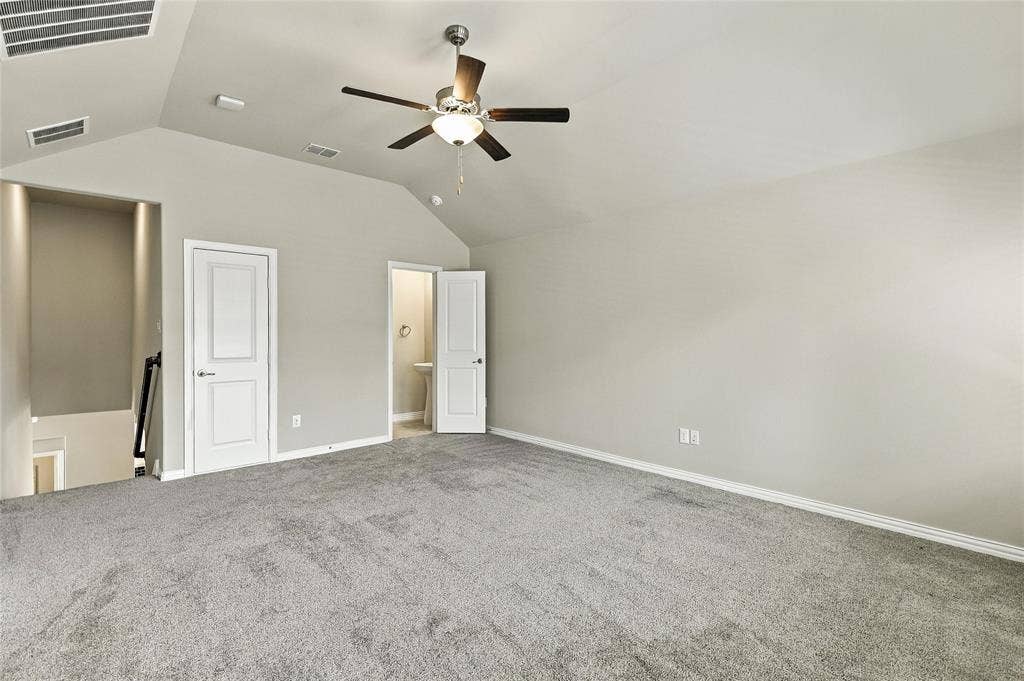 Vaulted ceiling featuring a central multi-blade ceiling fan, neutral wall finishes, and carpeted flooring