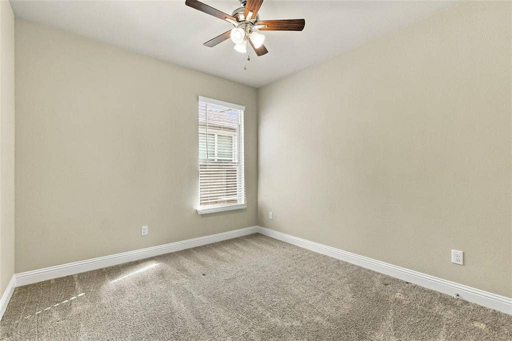 Neutral-toned interior featuring wall-to-wall carpeting, a multi-blade ceiling fan with integrated lighting, and a single-pane window with horizontal blinds