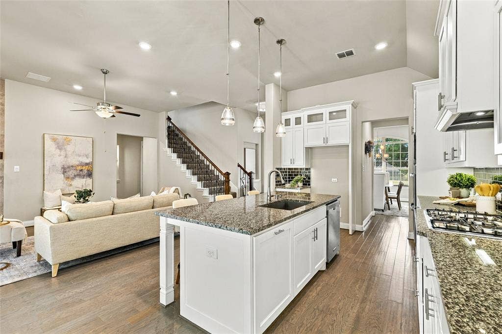 Kitchen featuring white shaker-style cabinetry, stone countertops, stainless steel appliances, wood-finish flooring, and pendant lighting