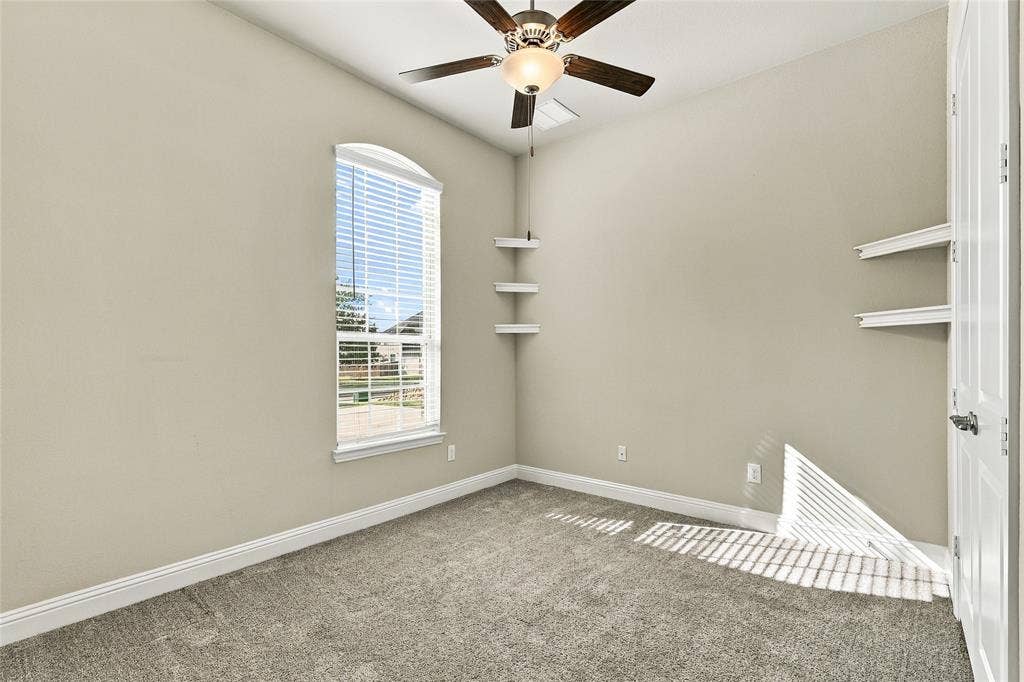 Room featuring an arched window, carpeted flooring, a ceiling fan with integrated lighting, and multiple built-in wall-mounted shelves