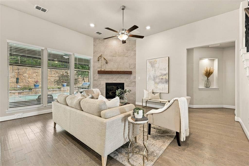 Living area featuring wood-finish flooring, a stone-surround fireplace with a timber mantel, a recessed wall niche, and large windows