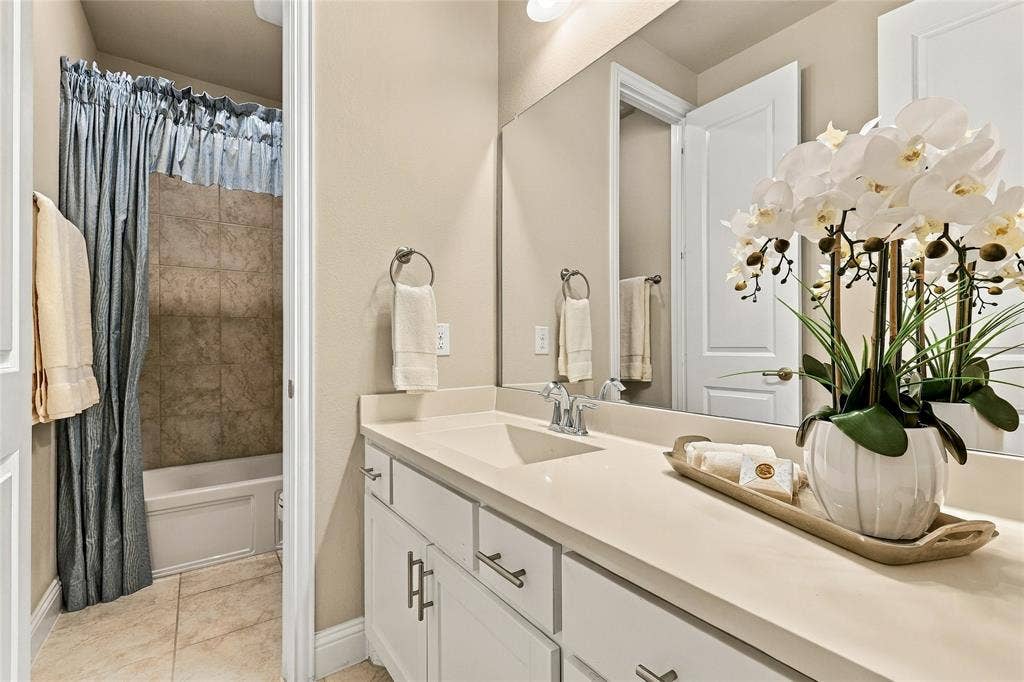 Bathroom featuring a vanity with a solid-surface countertop, an integrated sink, white cabinetry with brushed-metal pulls, and a full-width mirror