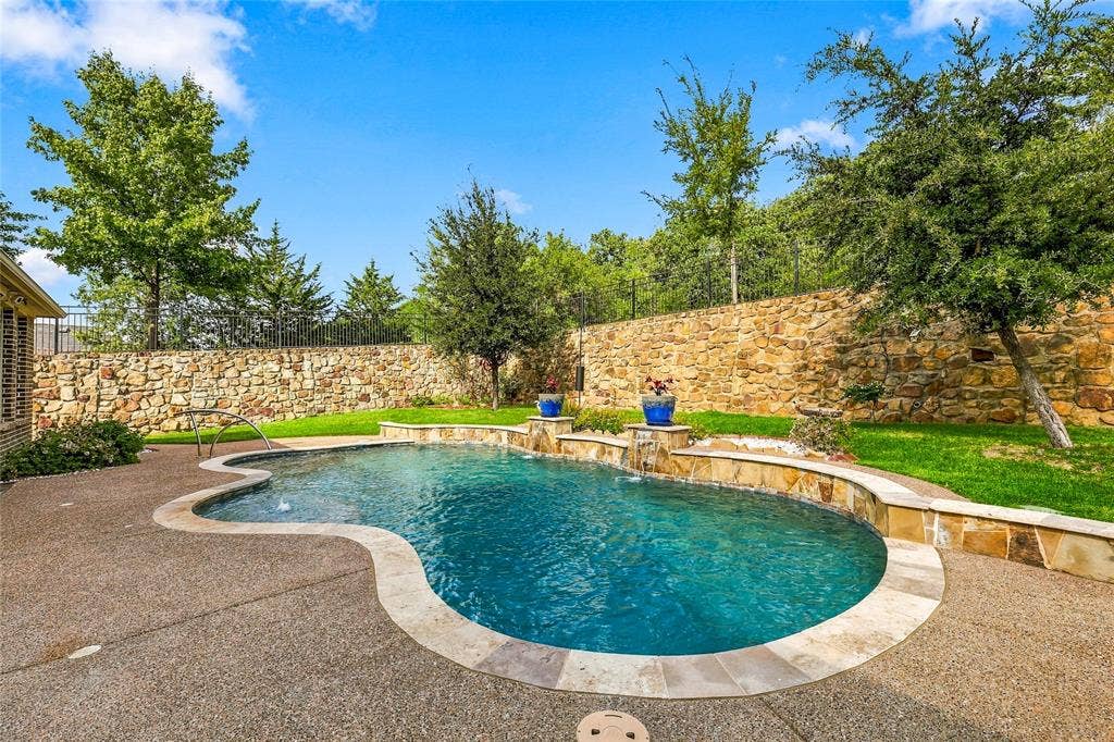 Freeform pool featuring stone water features, a concrete pool deck, and a surrounding natural stone privacy wall