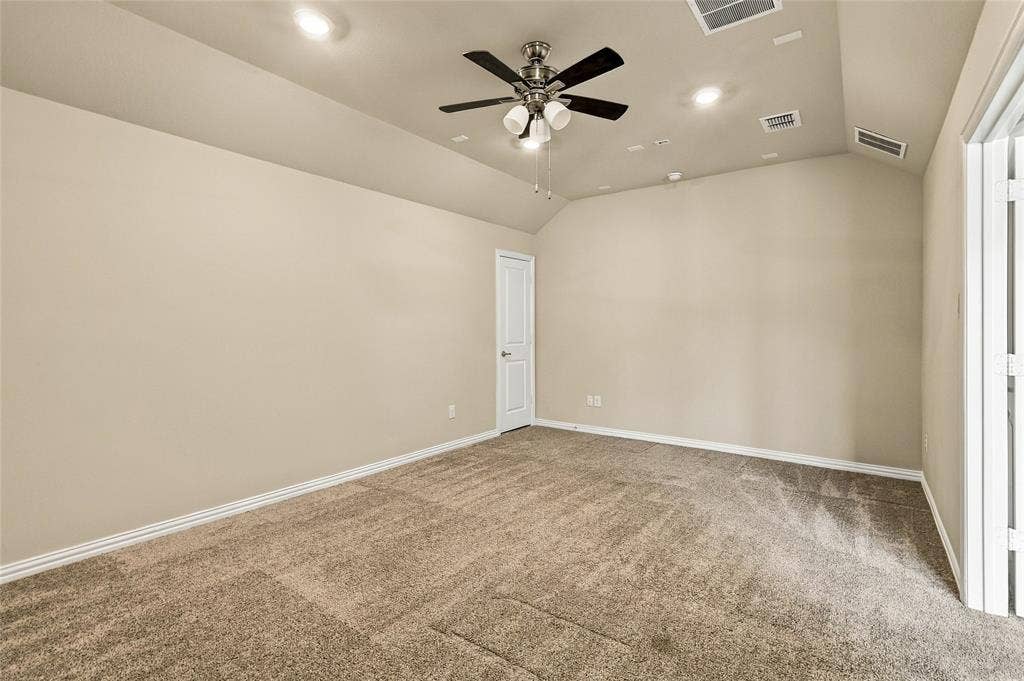 Interior space featuring vaulted ceilings, neutral wall tones, textured carpeting, a multi-blade ceiling fan with integrated lighting, and recessed overhead illumination