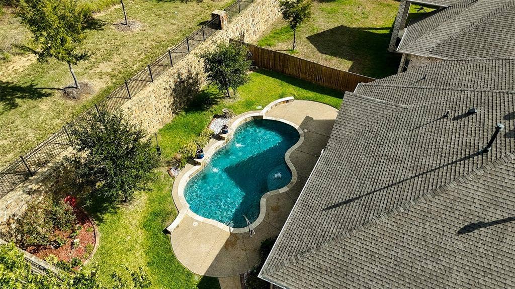 Backyard featuring a freeform swimming pool, concrete decking, stone perimeter fencing, and mature landscaping