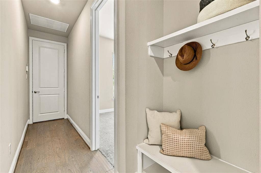 Built-in wall-mounted shelving unit with integrated coat hooks, recessed ceiling lighting, wood-finish flooring, and a solid-core panel door