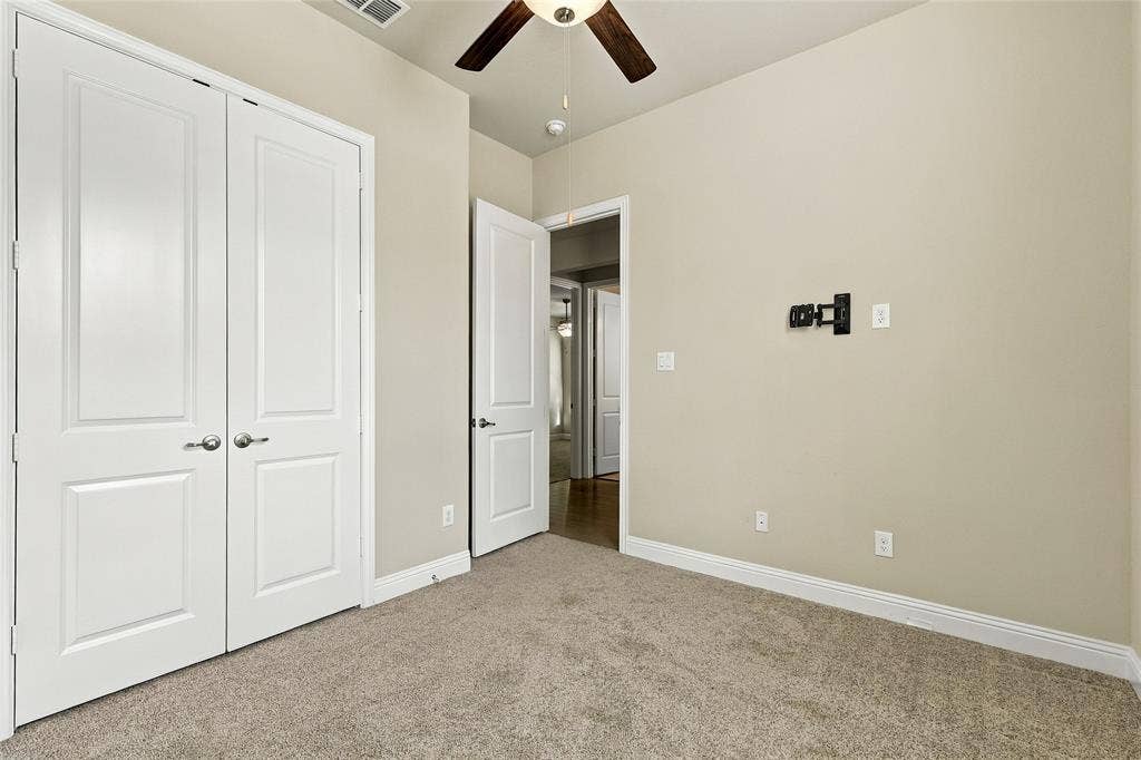 Neutral wall tones, wall-to-wall carpeting, ceiling fan with integrated lighting, two-panel interior doors, and a wall-mounted television bracket