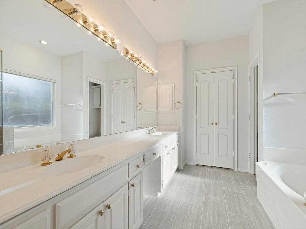 2817 Mayfair Lane, McKinney, TX 75071 Bathroom featuring a dual-sink vanity with a countertop, expansive wall-to-wall mirror, multi-bulb overhead lighting, and porcelain tile flooring
