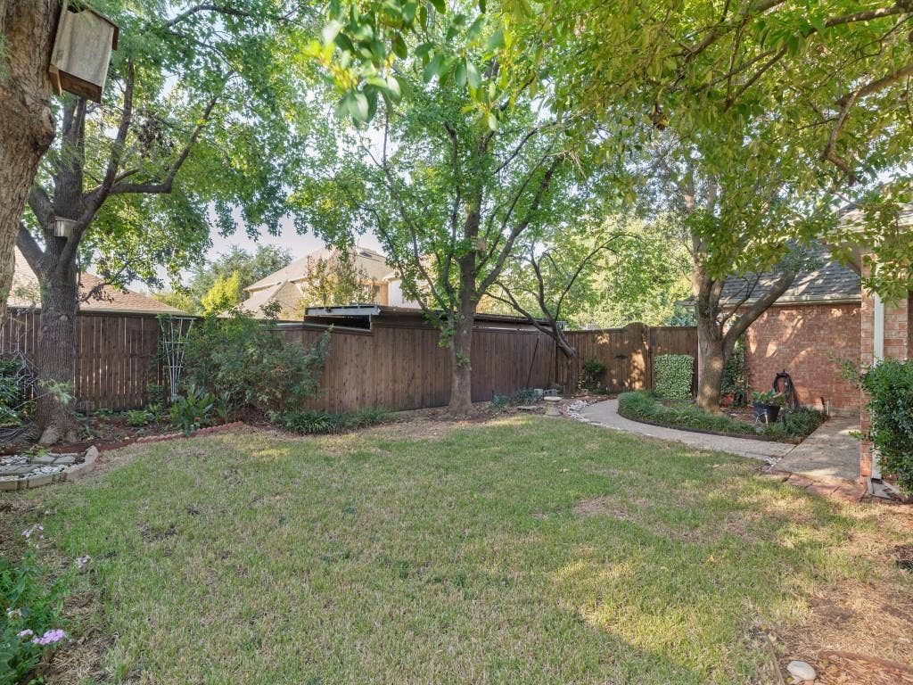 2817 Mayfair Lane, McKinney, TX 75071 Backyard featuring a grass lawn, mature trees, wood privacy fencing, and a stone-paver walkway