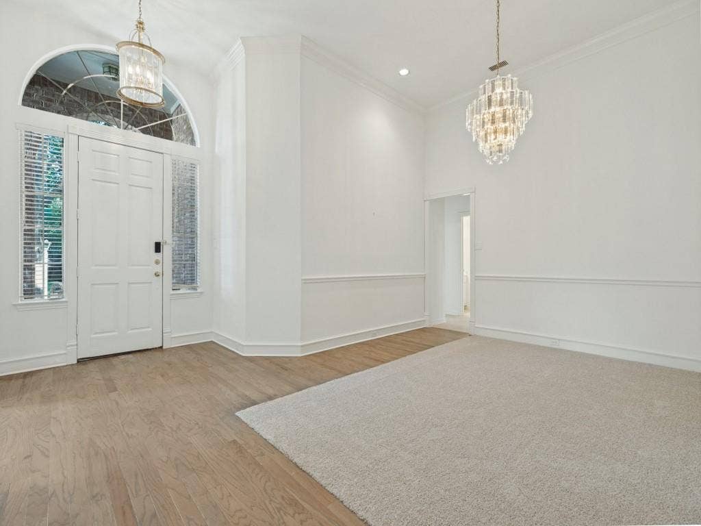2817 Mayfair Lane, McKinney, TX 75071 Entrance featuring an arched transom window, crystal-style chandeliers, decorative chair rail molding, wood-finish flooring, and wall-to-wall carpeting