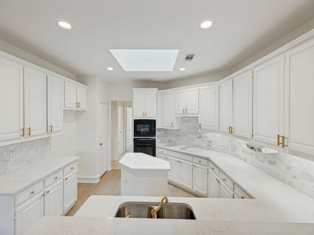 2817 Mayfair Lane, McKinney, TX 75071 Kitchen featuring white shaker-style cabinetry, solid-surface countertops, a center island, recessed ceiling lighting, and a skylight
