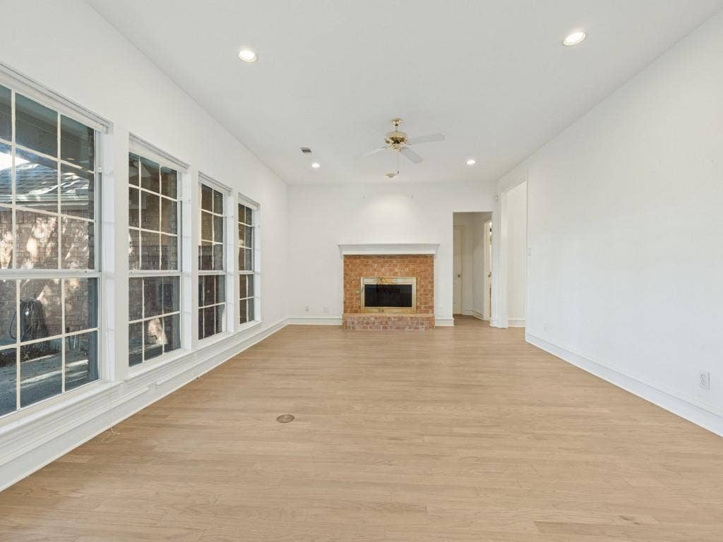 2817 Mayfair Lane, McKinney, TX 75071 Open-concept interior featuring light wood-finish flooring, recessed lighting, grid-pattern windows, and a masonry fireplace with a white mantel