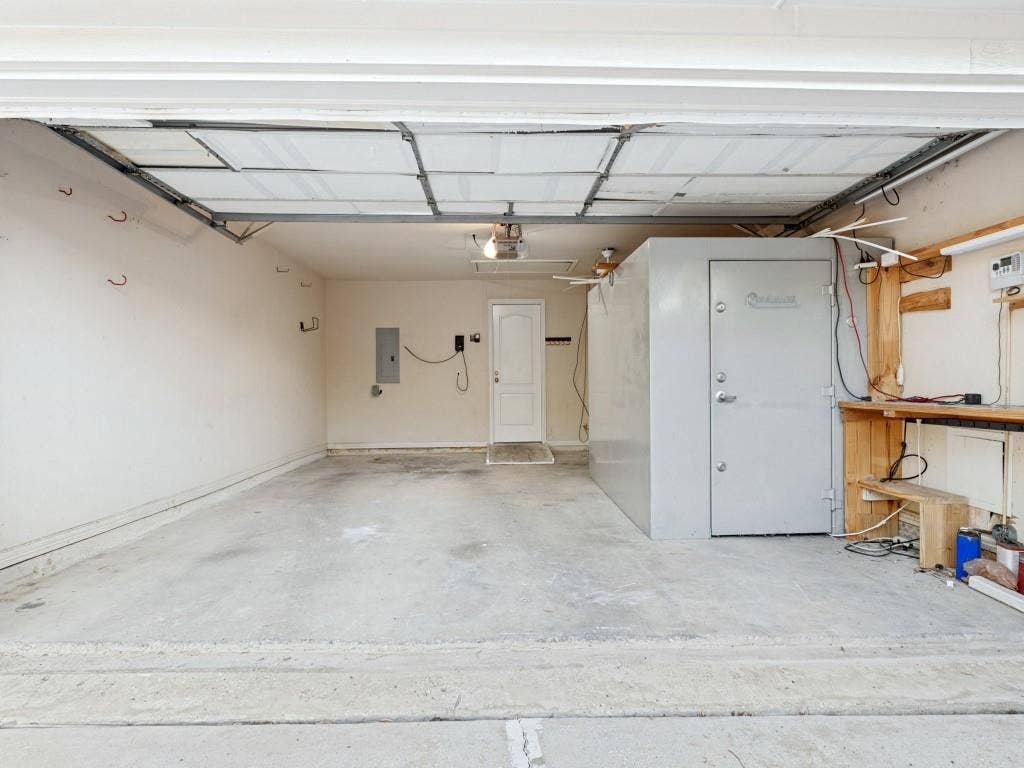 2817 Mayfair Lane, McKinney, TX 75071 Multi-car garage featuring a concrete floor, overhead door, built-in metal storage vault, and integrated wooden workbench