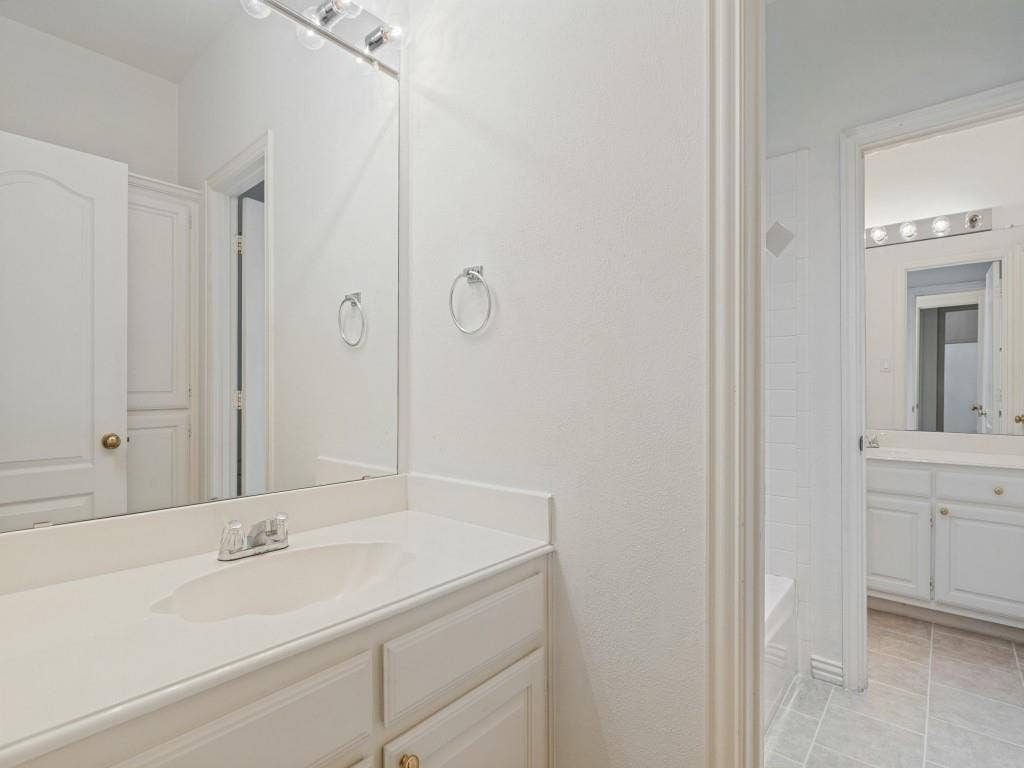 2817 Mayfair Lane, McKinney, TX 75071 White vanity cabinetry with a solid surface countertop, integrated sink, full-width vanity mirror, and tile flooring