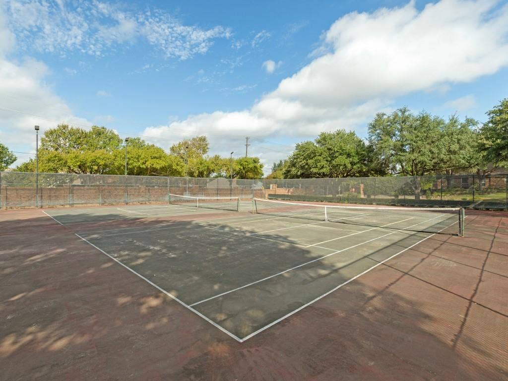 2817 Mayfair Lane, McKinney, TX 75071 Dual outdoor tennis courts featuring perimeter chain-link fencing, structural lighting poles, and mature tree boundaries