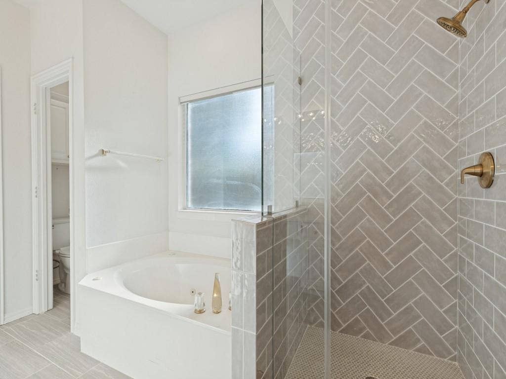 2817 Mayfair Lane, McKinney, TX 75071 Shower enclosure featuring herringbone-patterned wall tile, frameless glass door, and metallic finish fixtures, complemented by a built-in soaking tub