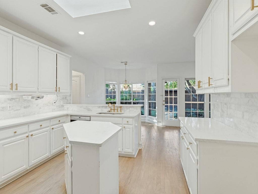 2817 Mayfair Lane, McKinney, TX 75071 Kitchen featuring white cabinetry with gold-tone hardware, light-toned countertops, stone tile backsplash, wood-finish flooring, and a multi-sided center island