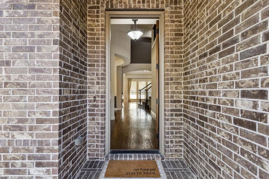 6448 Fire Creek Trail, Frisco, TX 75036 Exterior entrance featuring multi-tonal brick masonry, wood-finish flooring, and a pendant light fixture