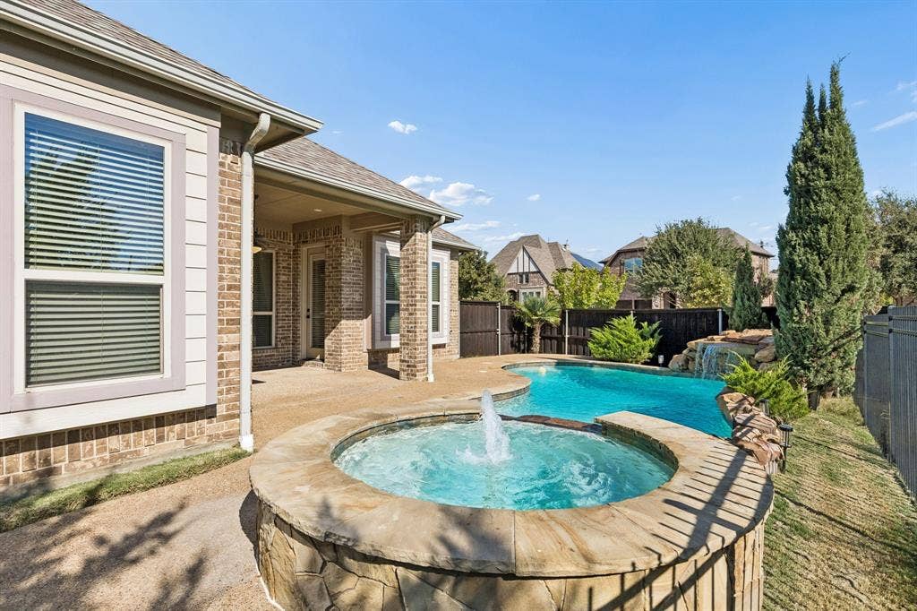 6448 Fire Creek Trail, Frisco, TX 75036 Brick and siding exterior featuring a covered patio, a stone-accented hot tub with a water feature, and a custom-shaped swimming pool