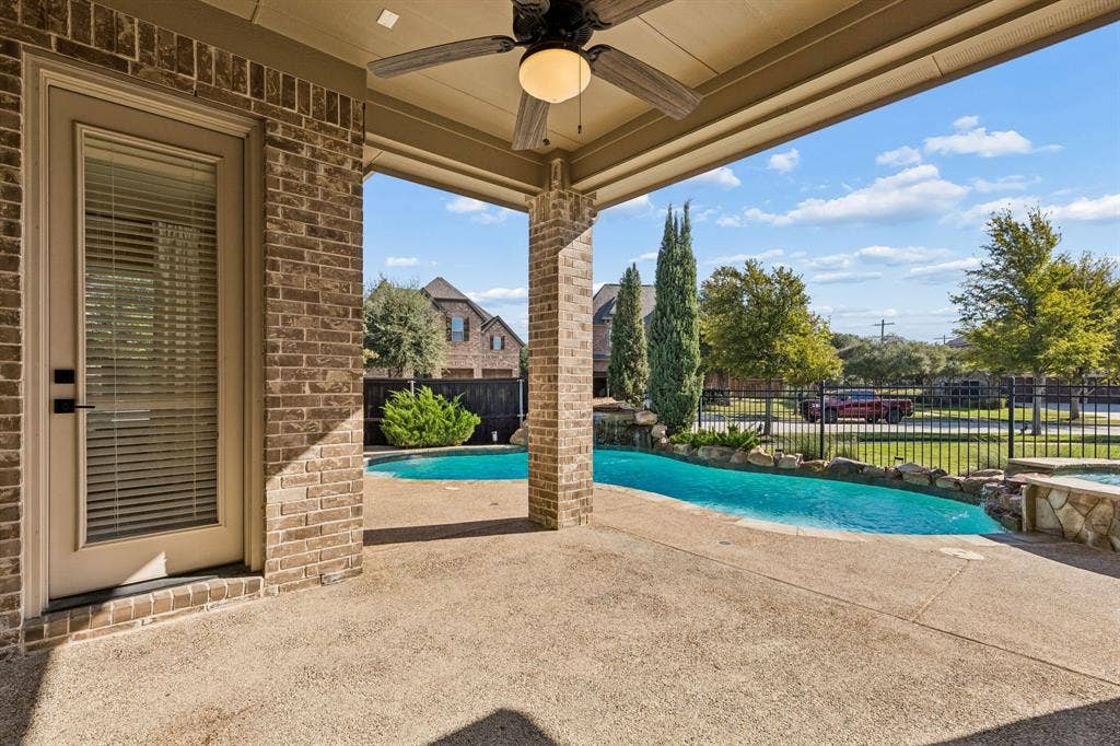 6448 Fire Creek Trail, Frisco, TX 75036 Covered patio featuring a brick exterior, recessed ceiling, and an integrated overhead fan, overlooking an in-ground pool with a stone-accented spa and perimeter metal fencing