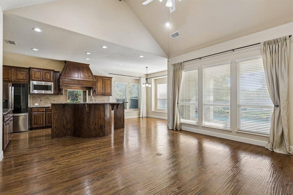 6448 Fire Creek Trail, Frisco, TX 75036 Vaulted ceiling, wood-finish flooring, custom wood cabinetry, central kitchen island, and expansive windows