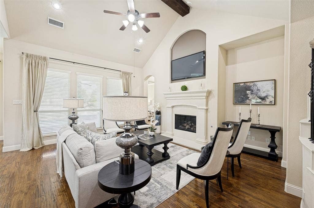 6448 Fire Creek Trail, Frisco, TX 75036 Vaulted ceiling featuring a decorative wood beam, stone-surround fireplace with a recessed alcove, large windows with multi-pane configuration, and wood-finish flooring