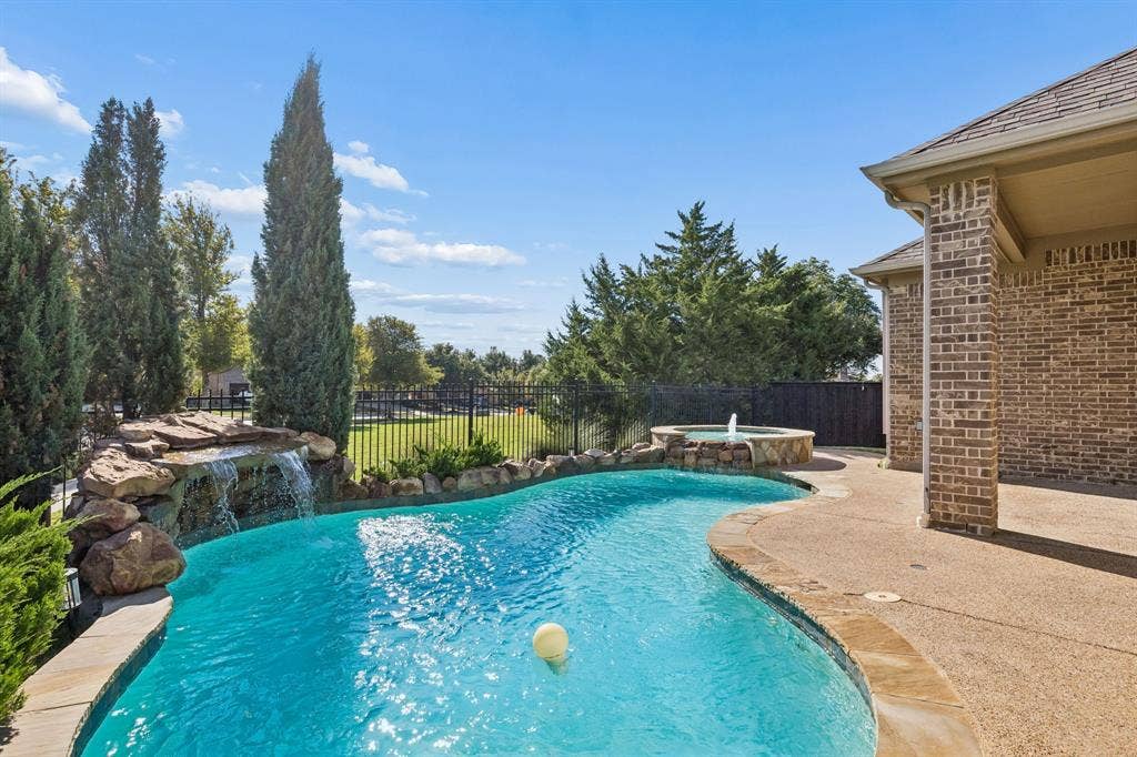 6448 Fire Creek Trail, Frisco, TX 75036 Outdoor pool area featuring a natural rock waterfall, elevated spill-over spa, textured concrete decking, and brick exterior finish