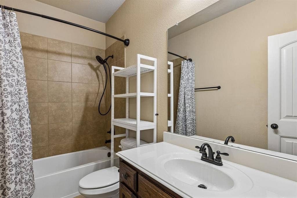 6448 Fire Creek Trail, Frisco, TX 75036 Bathroom featuring a vanity with a white countertop and oval under-mount sink, dark wood-finish cabinetry, matte black hardware, and a shower-tub combination with tiled surround