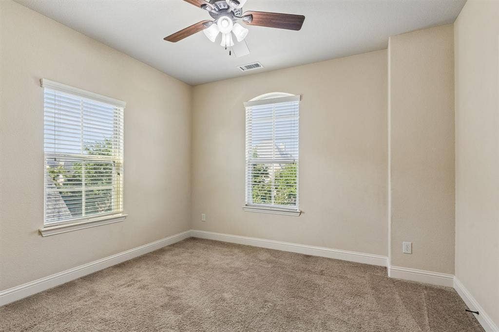 6448 Fire Creek Trail, Frisco, TX 75036 Interior space featuring neutral wall tones, carpeted flooring, two double-hung windows with arched upper panes, and a ceiling fan with integrated lighting