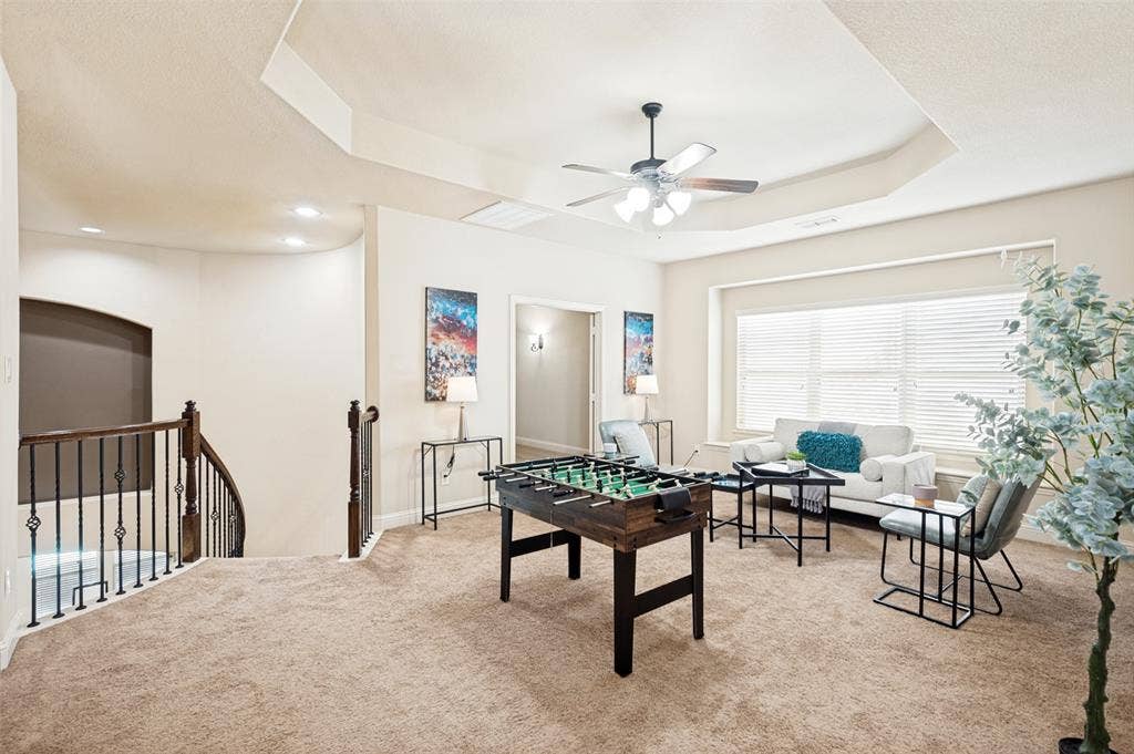 6448 Fire Creek Trail, Frisco, TX 75036 Tray ceiling with a central ceiling fan, windowed wall with horizontal blinds, and a staircase featuring a wooden handrail and metal balusters