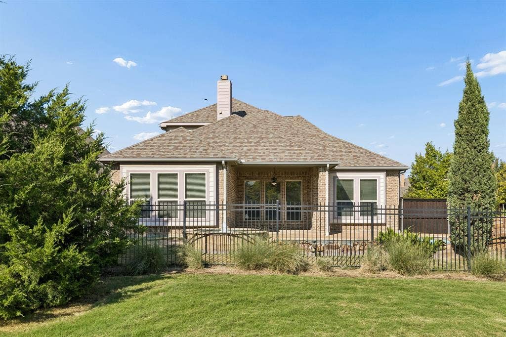 6448 Fire Creek Trail, Frisco, TX 75036 Rear elevation featuring a brick exterior, gabled roofline, centralized masonry chimney, covered patio, and perimeter metal fencing
