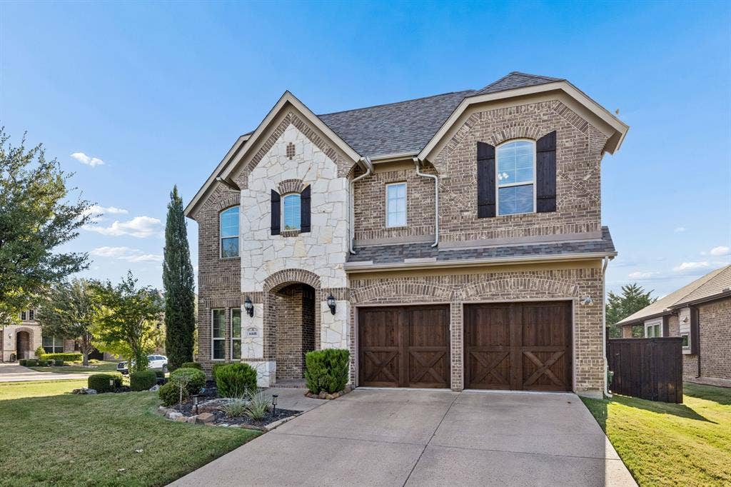 6448 Fire Creek Trail, Frisco, TX 75036 Two-story brick and stone facade featuring arched window detailing, dark-finished carriage-style garage doors, and decorative exterior shutters