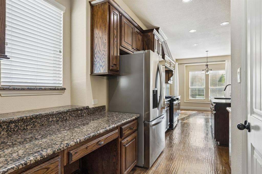 6448 Fire Creek Trail, Frisco, TX 75036 Kitchen area featuring wood-finish flooring, dark-stained cabinetry, stone countertops, and stainless steel appliances